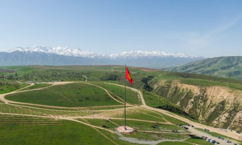 Kyrgyzstan flag waving on flagpole with snowy mountains in the background
